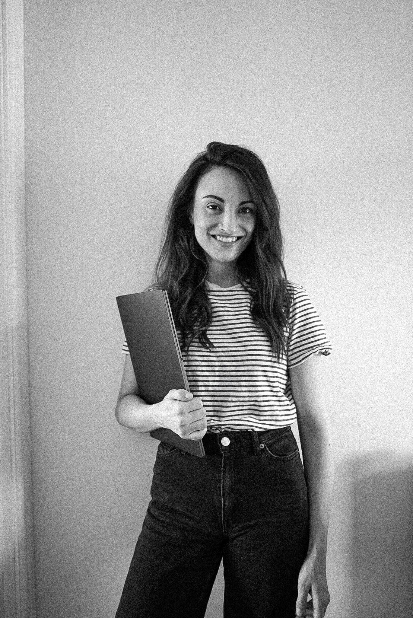 Black and white portrait of Carly, founder of Nightbloom Studio, smiling and holding a laptop
