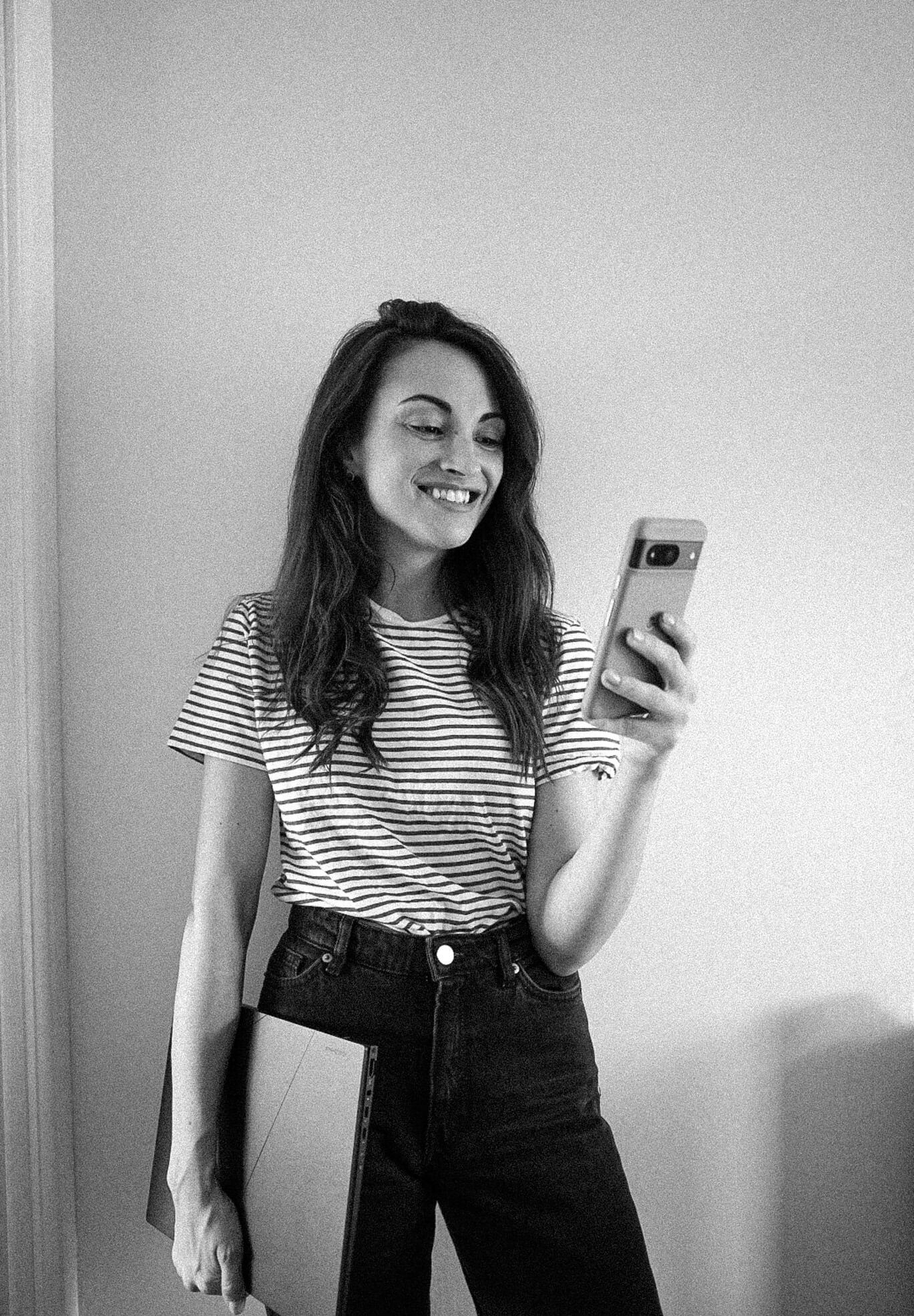 Black and white portrait of Carly smiling at her phone while holding a laptop