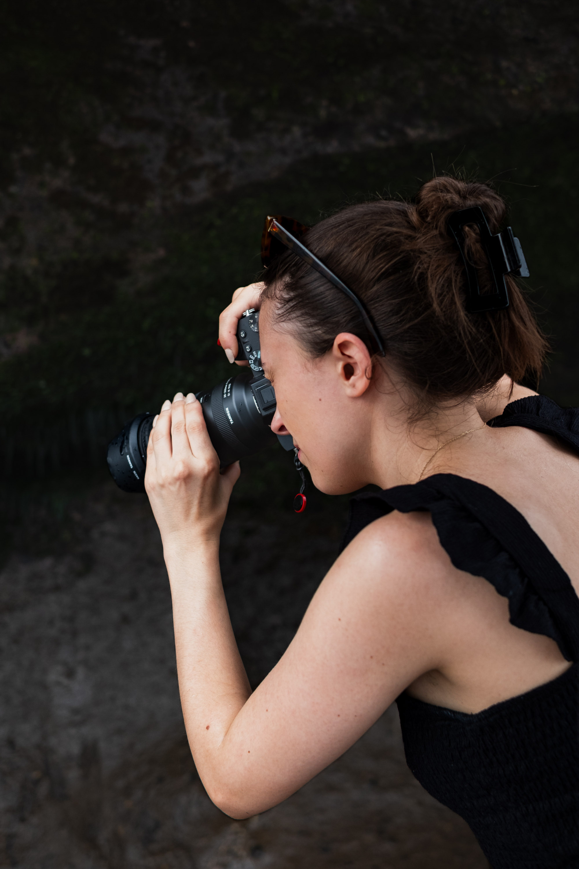 Carly being photographed from behind as she looks through a camera, sunglasses pushed up into her hair
