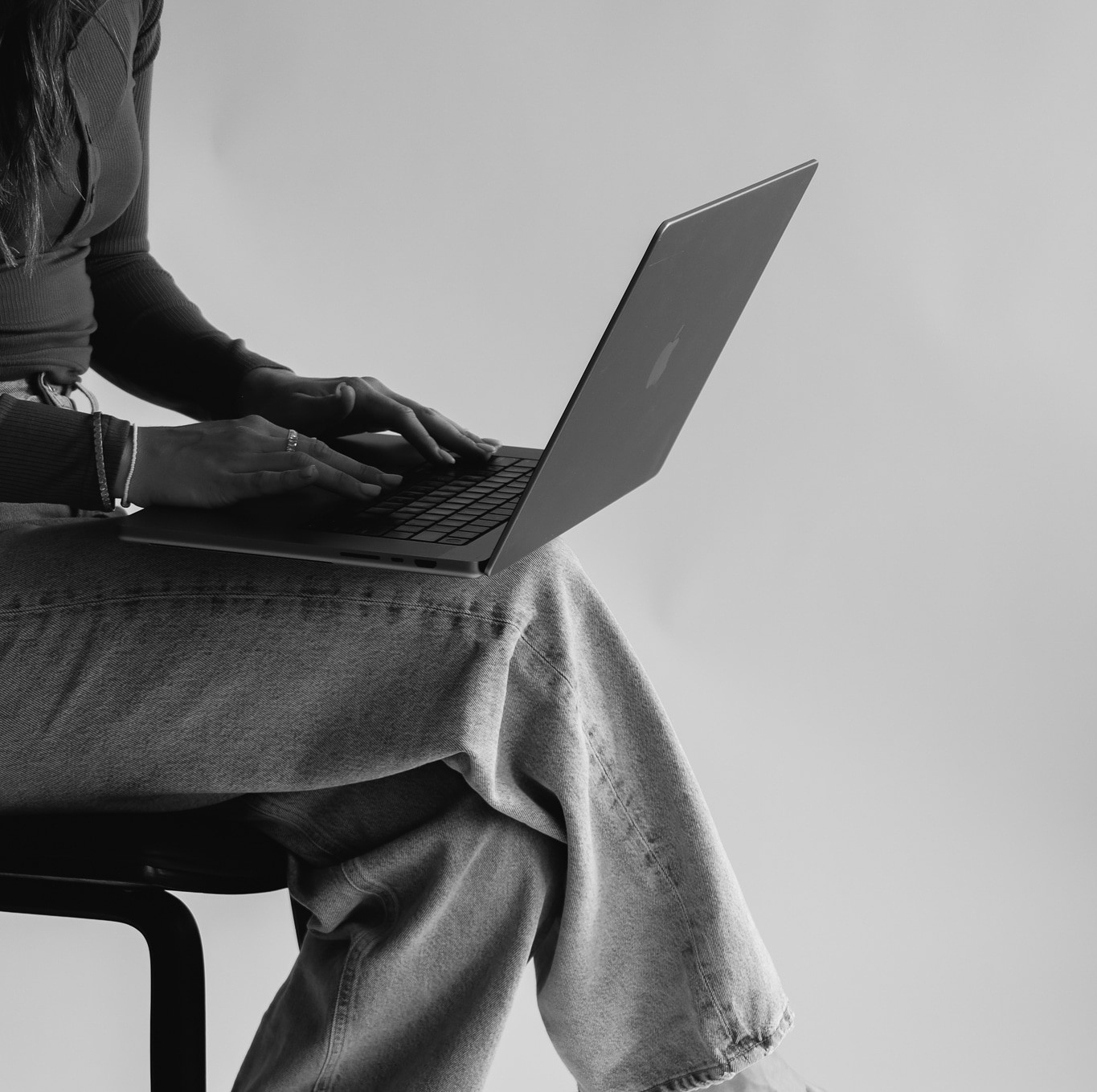 Black and white close-up of hands typing on a laptop, seated with legs crossed (closer crop)